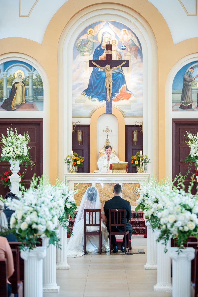 Bride and Groom sit at alter of church surrounded by white orchids