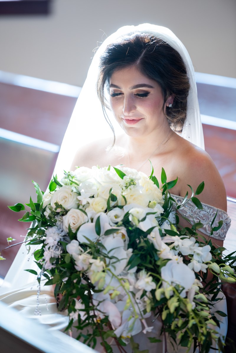 Light filters through bride's veil and white orchid bouquet