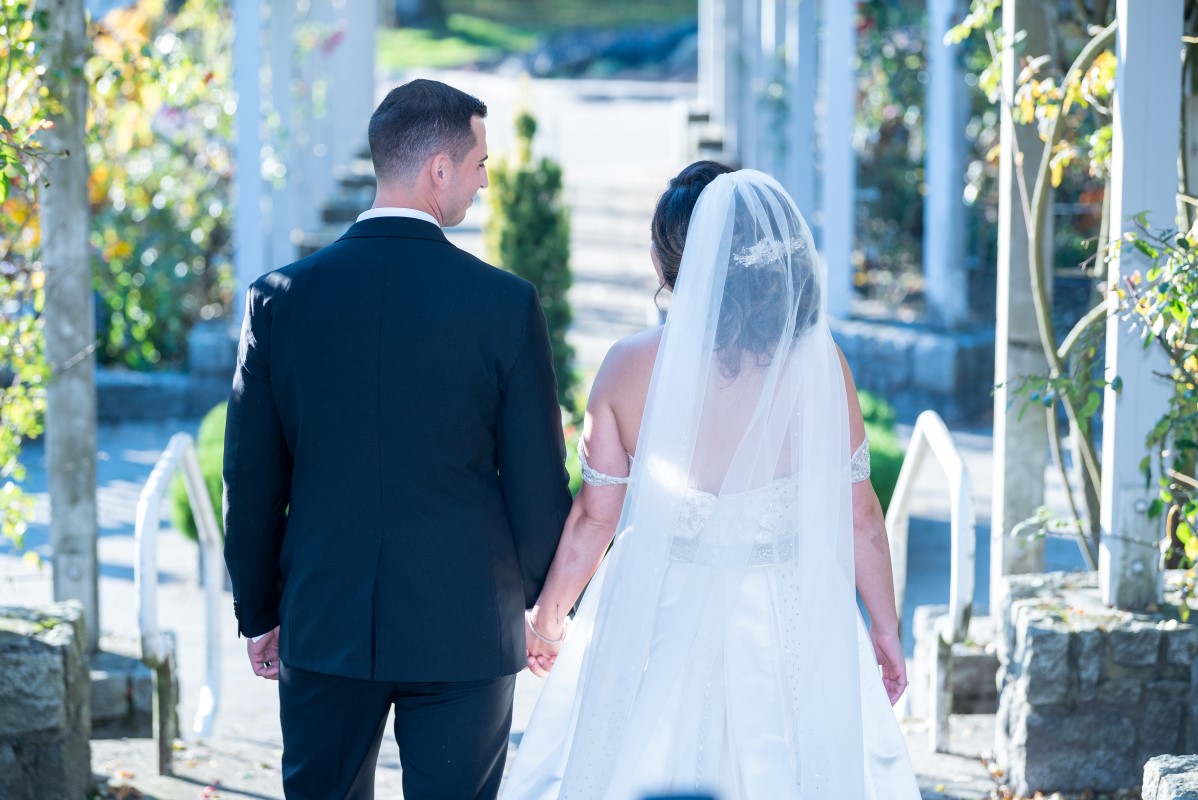 Bride and groom walk together holding handfs in a garden