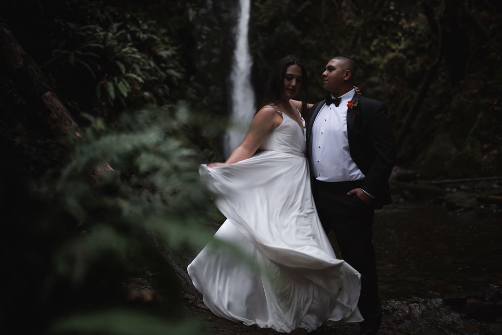 Bride twirls her dress and stands in front of waterfall with her groom