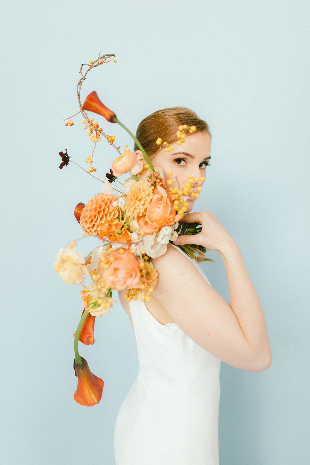 Vancouver Bride with red hair peeking behind her bouquet of orange dahlia and calla lily