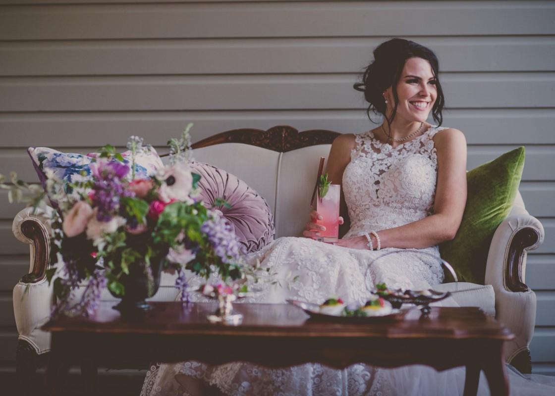 Bride enjoys drink on the deck filled with antique furniture and flowers