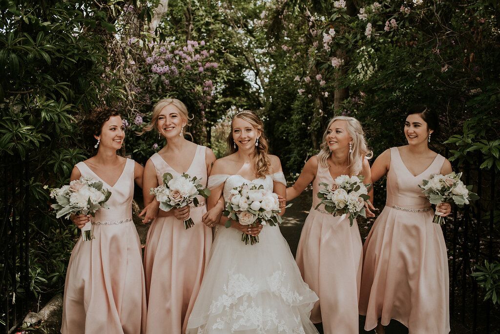 Romantic Bridesmaids in blush pink gowns carrying bouquets of peonies and roses