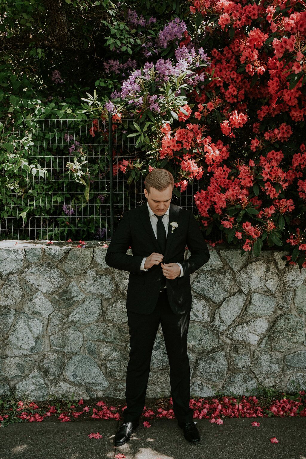 Groom buttons jacket of Indochino suit with pink flowers behind him