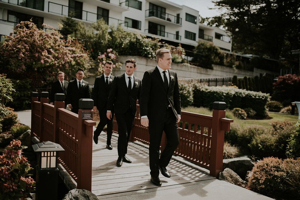 Groom and groomsman walk towards ceremony through garden bridge West Coast Weddings Magazine