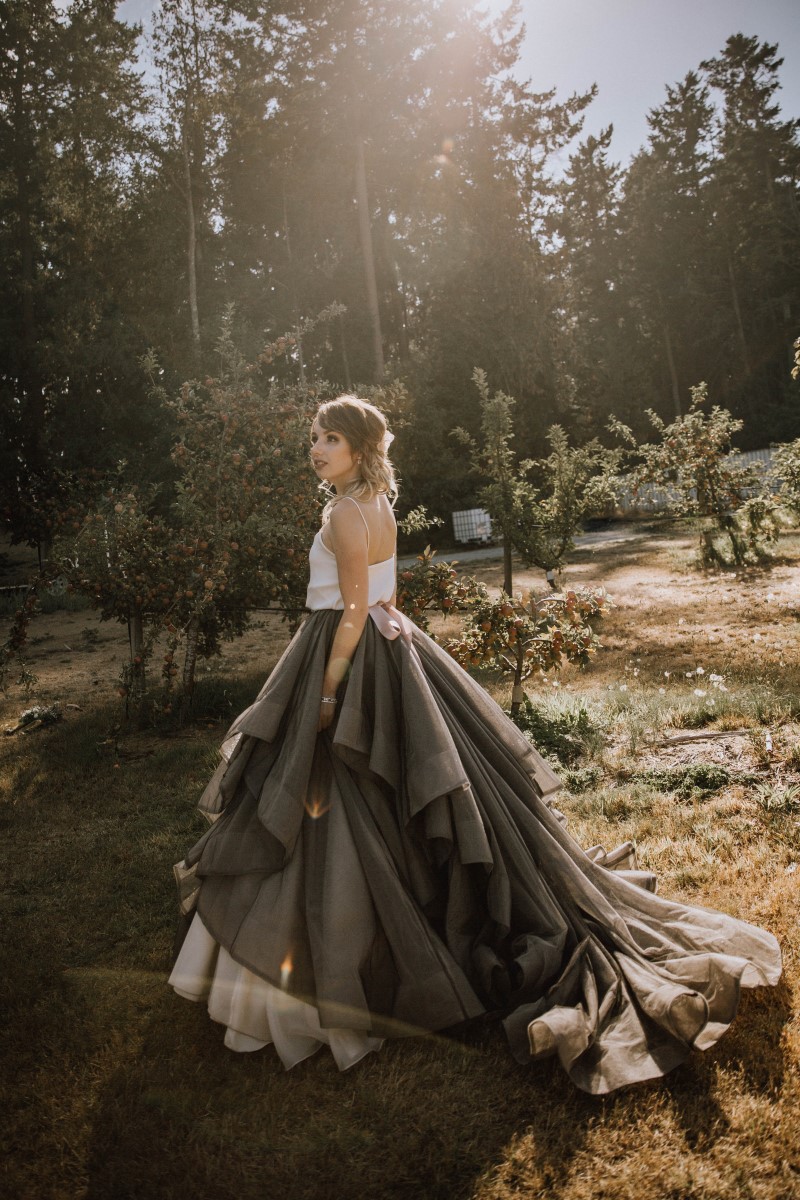 Bride in grey blue overskirt walks through orchard on Vancouver Island