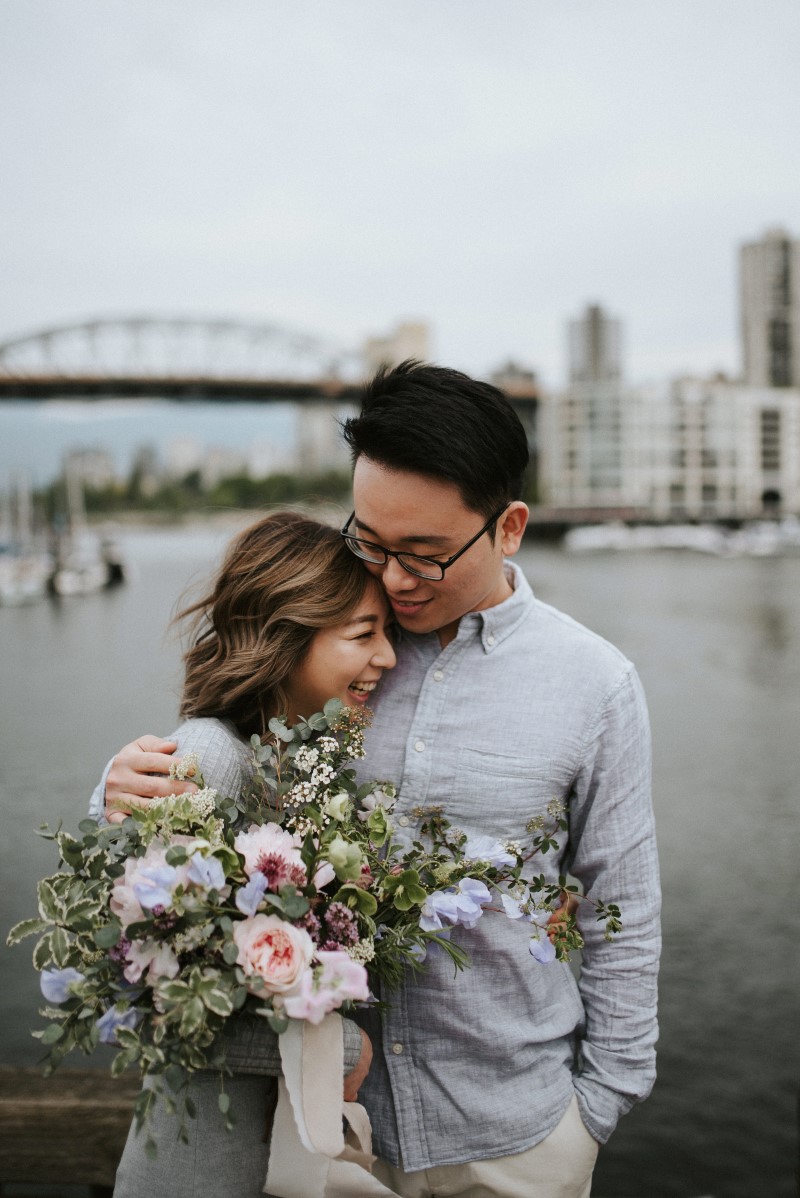 Vancouver Engagement Photo of couple in front of waterfront with bouquet West Coast Weddings Magazine