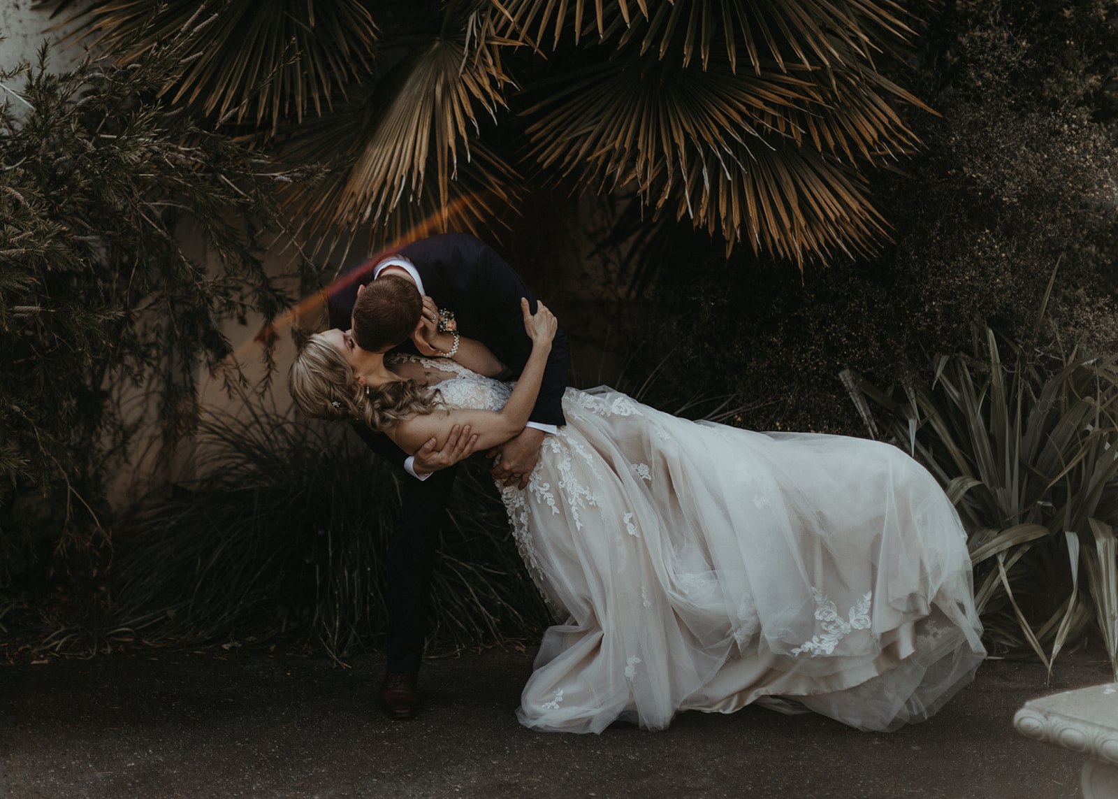 Groom dips bride as they kiss with palms behind them