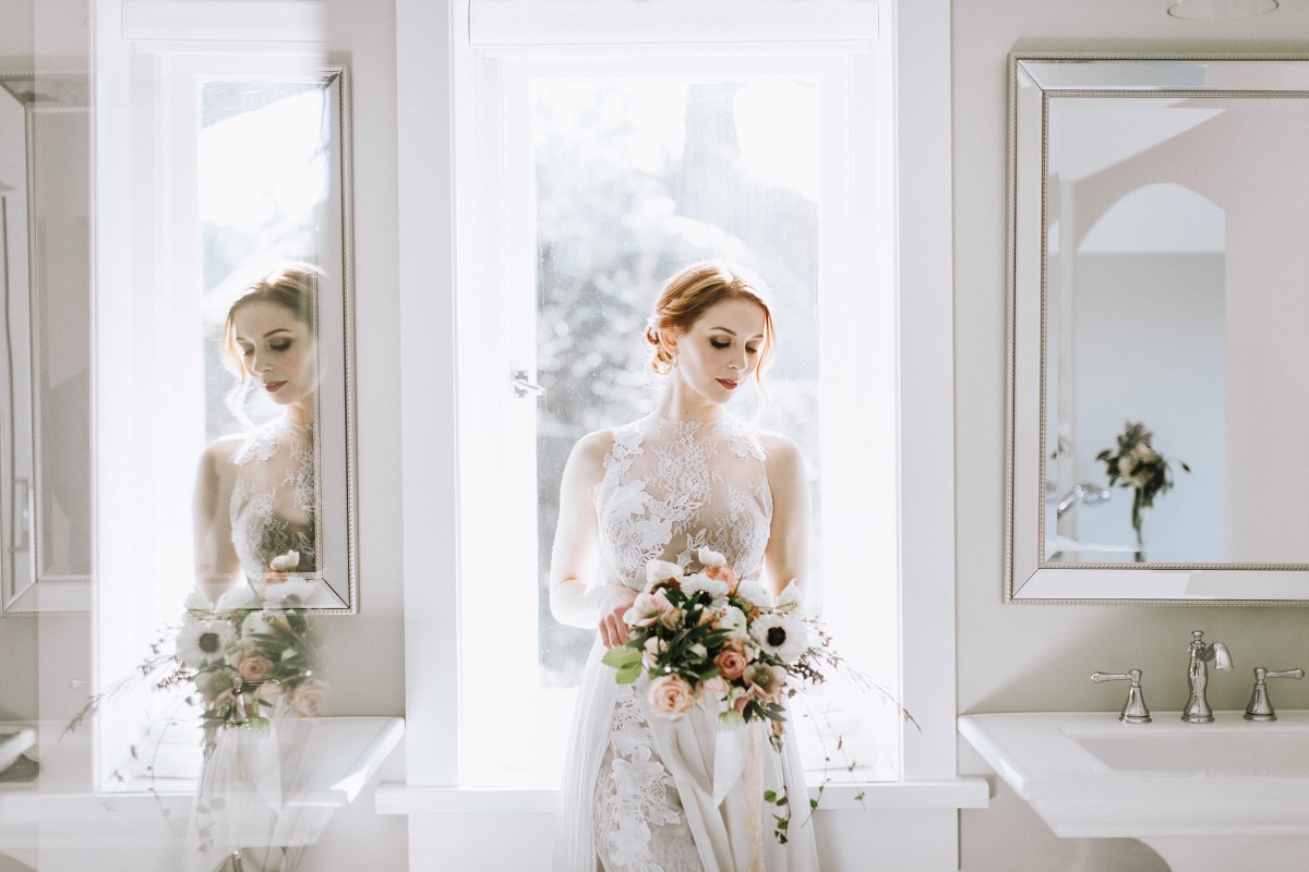 Bride in front of window with gorgeous bouquet by Fleur de Lil Vancouver Island