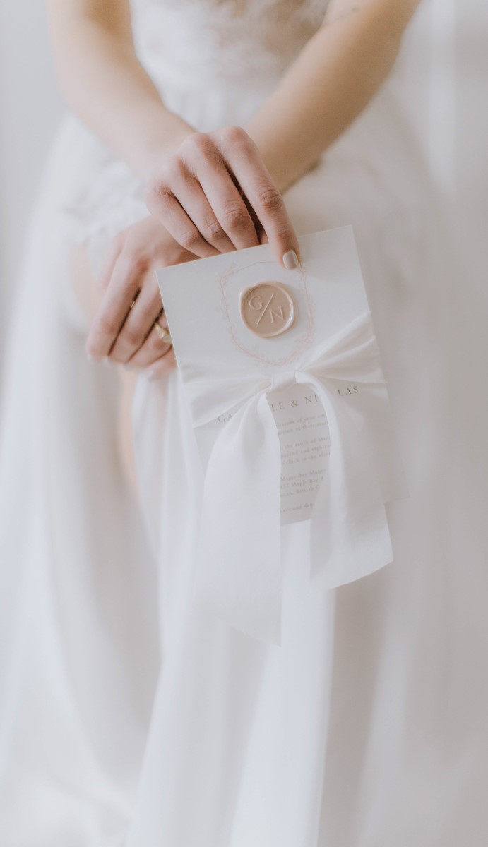 Bride holds white invitation suite with gold wax seal and white ribbon