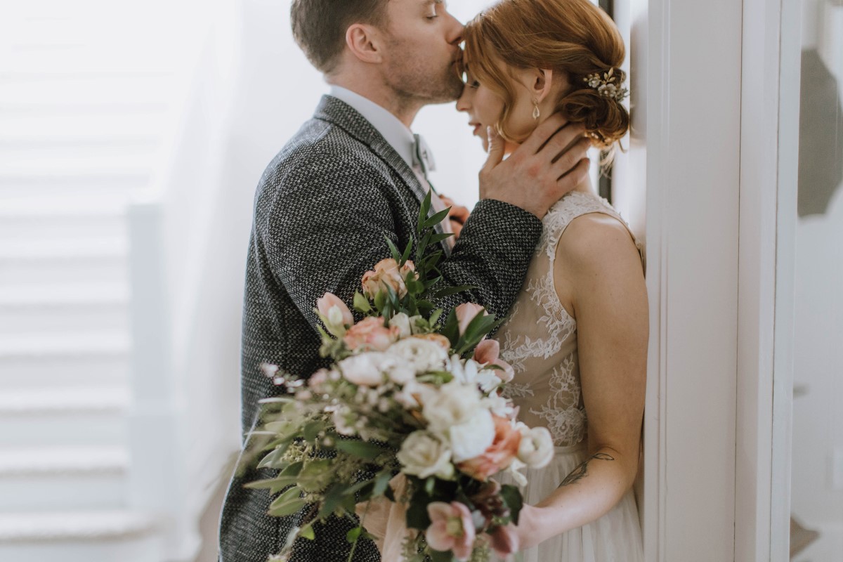 Groom in grey suit kisses bride's forehead