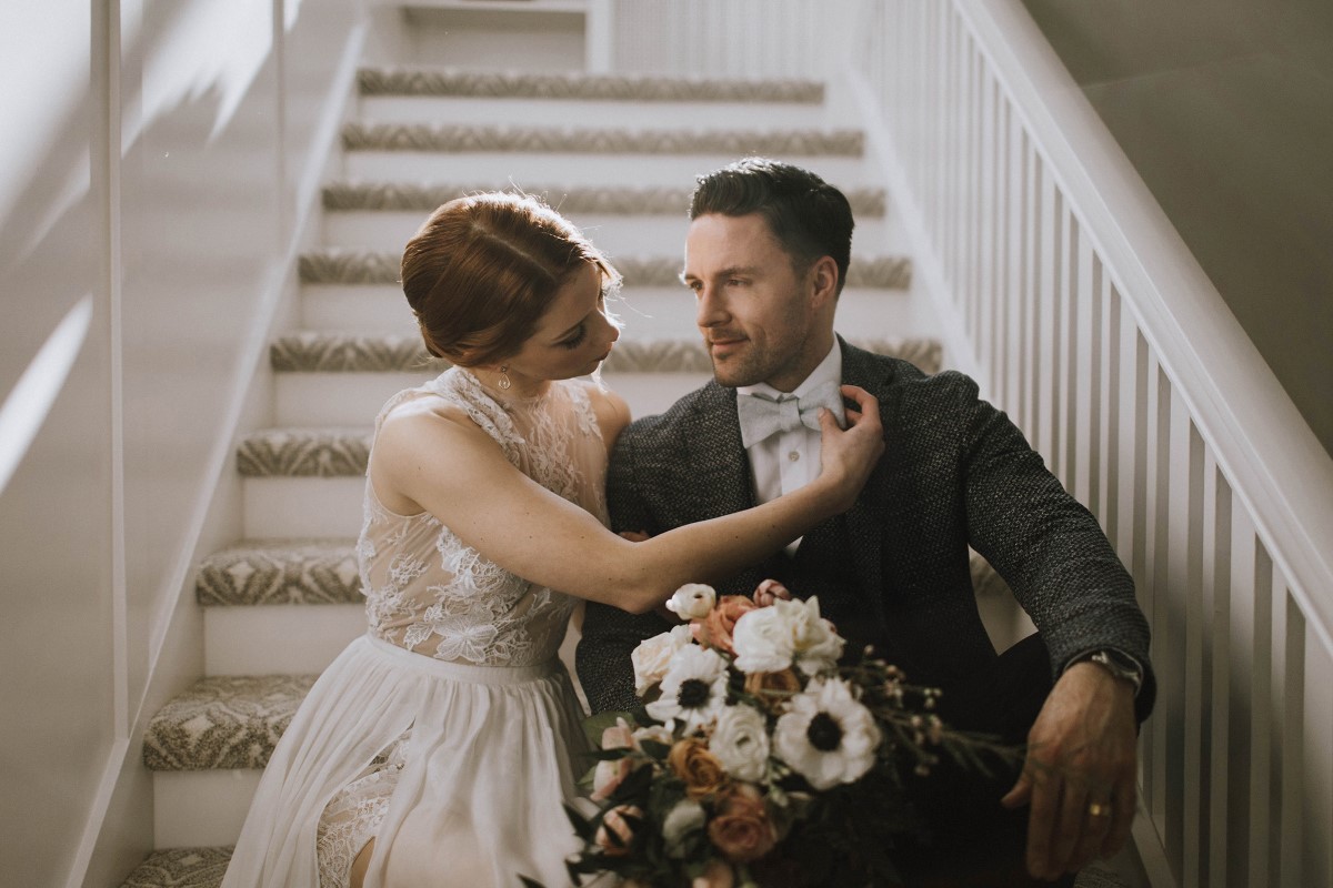 Newlyweds sit on a staircase and hold bridal bouquet at Maple Bay Manor