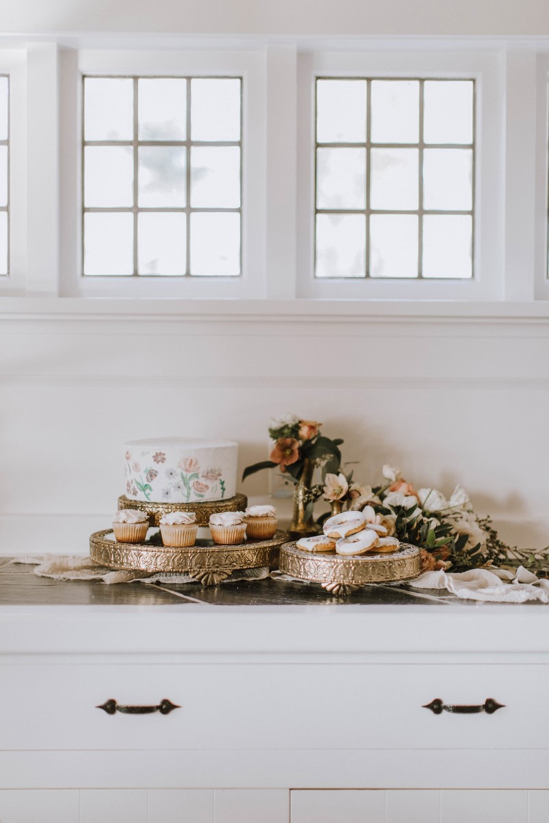 Wedding cake on dessert table with cookies, doughtnuts and floral against white walls