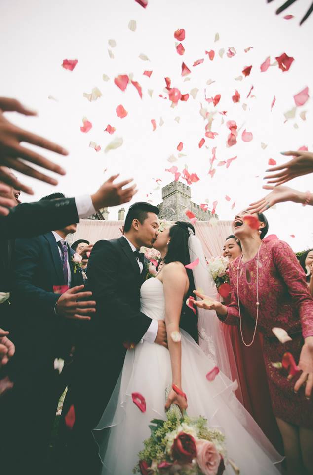 Newlyweds kissing surrounded by family throwing rose petals