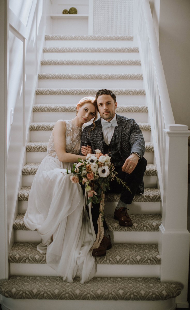 Newlyweds sit on stairs with bouquet West Coast Weddings Magazine