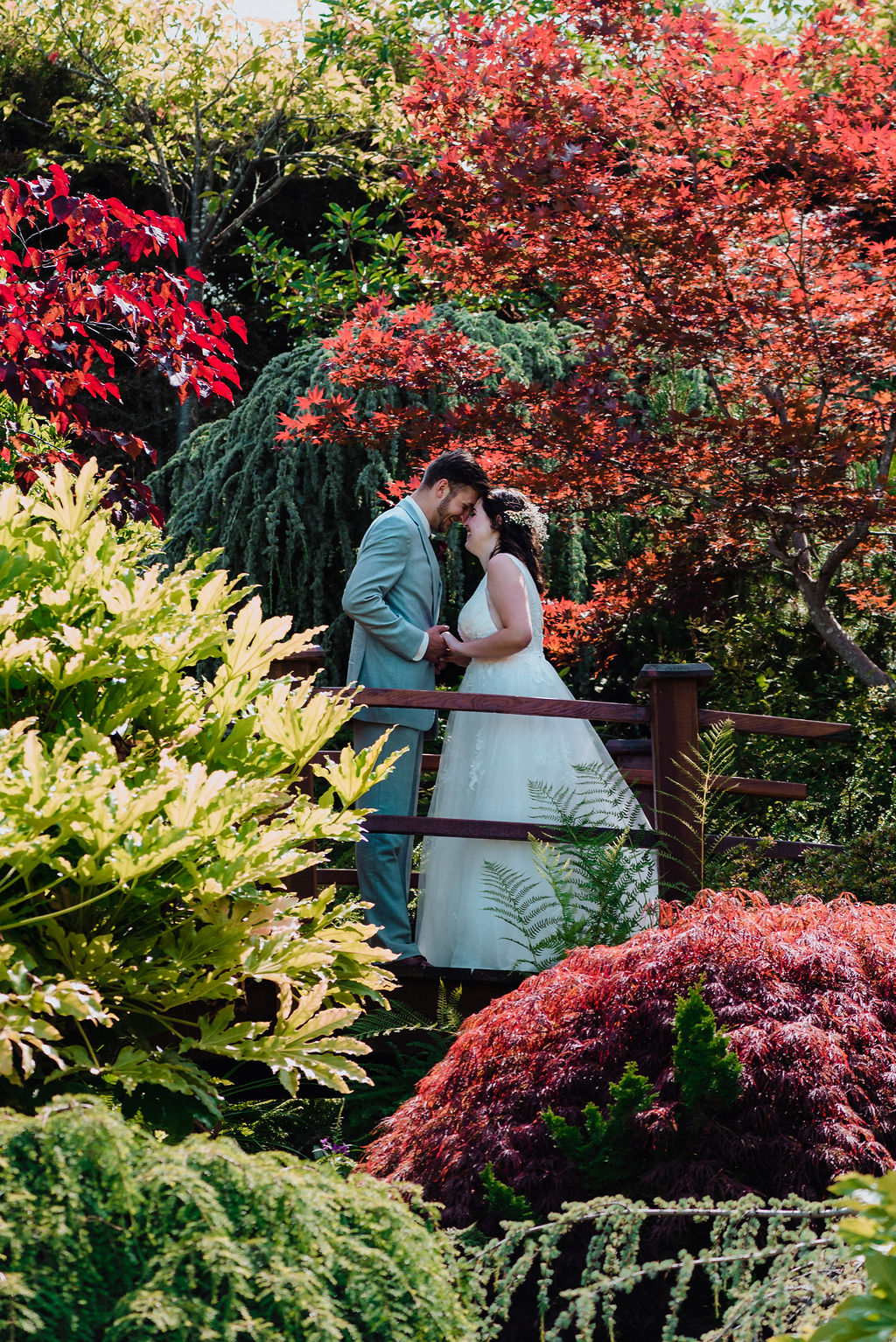 Newlyweds on foot bridge in garden of red and yellow bushes on Vancouver Island