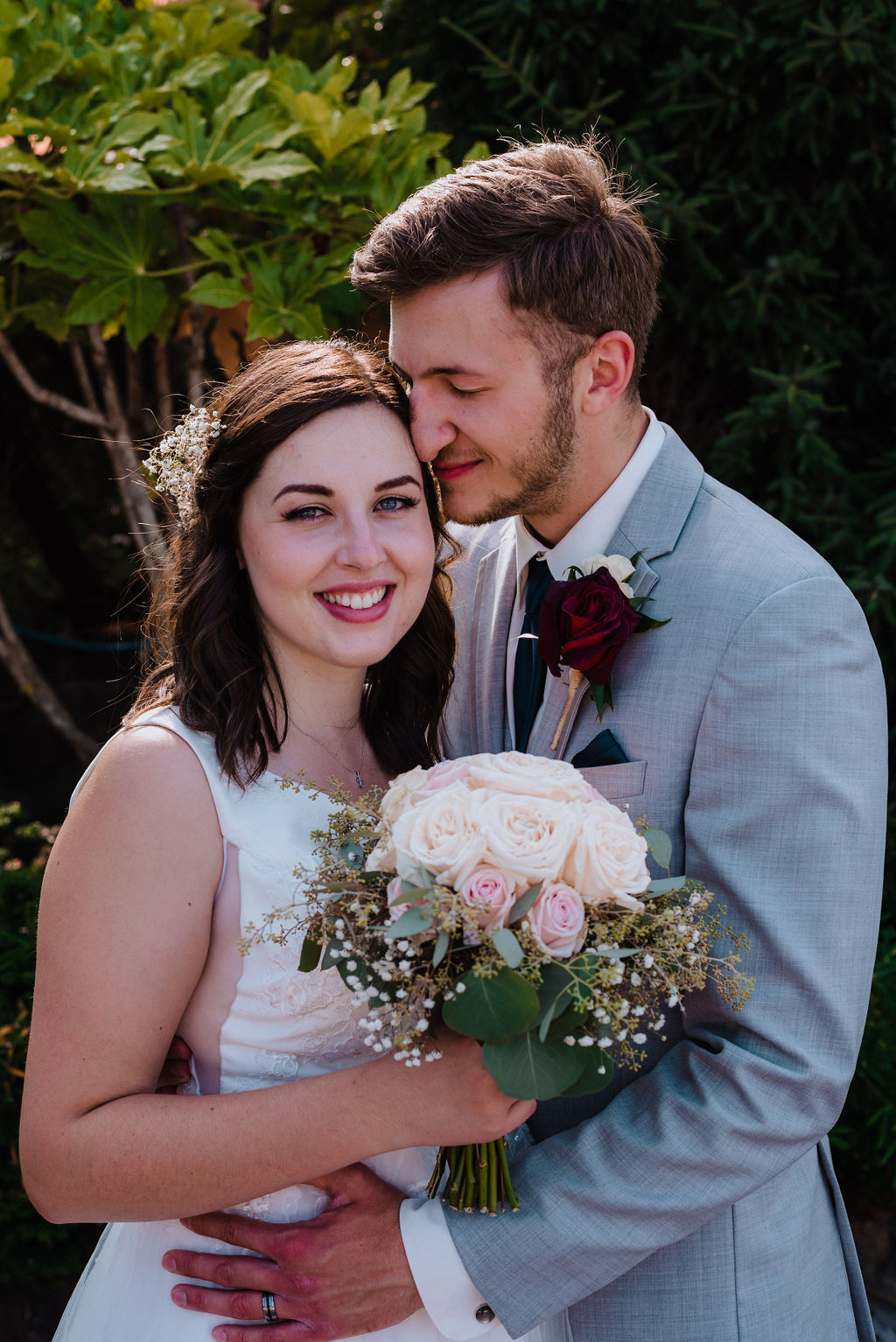 Bride smiles and holds bouquet while groom in grey suit holds her