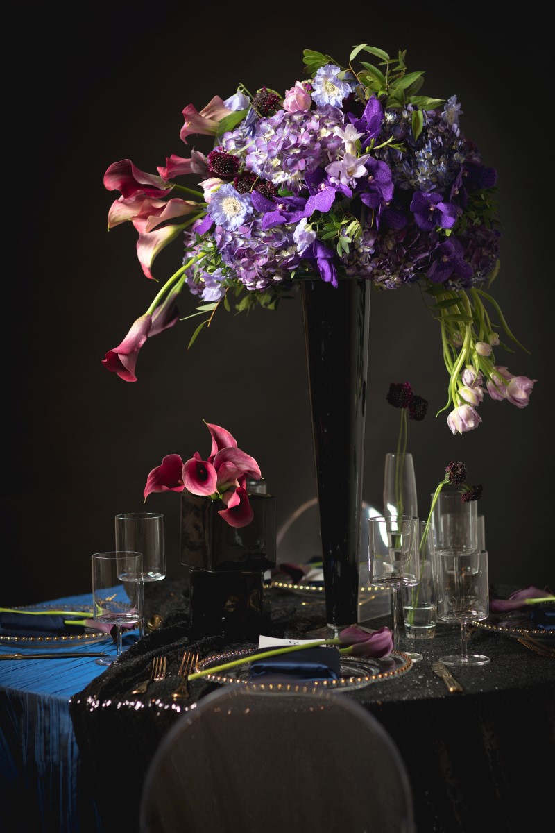 Dark blue linens on wedding reception table and large purple, blue and burgundy floral display