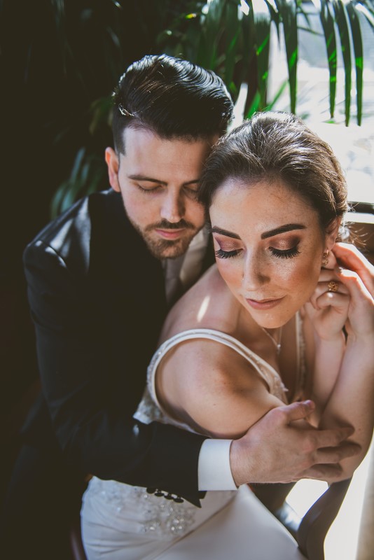 Bride with gorgeous makeup by Artistry by Alexa is held closely by groom at Fairmont Empress