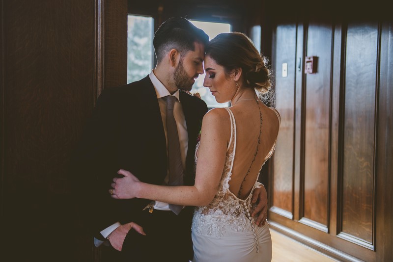 Groom wearing tux by Moore's Clothing holds bride in low back gown with tattoo at Fairmont Empress