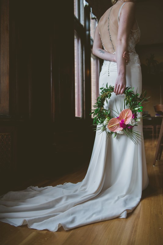 Bride holds hoop covered in greenery and coral flowers by Brown's the Florist 