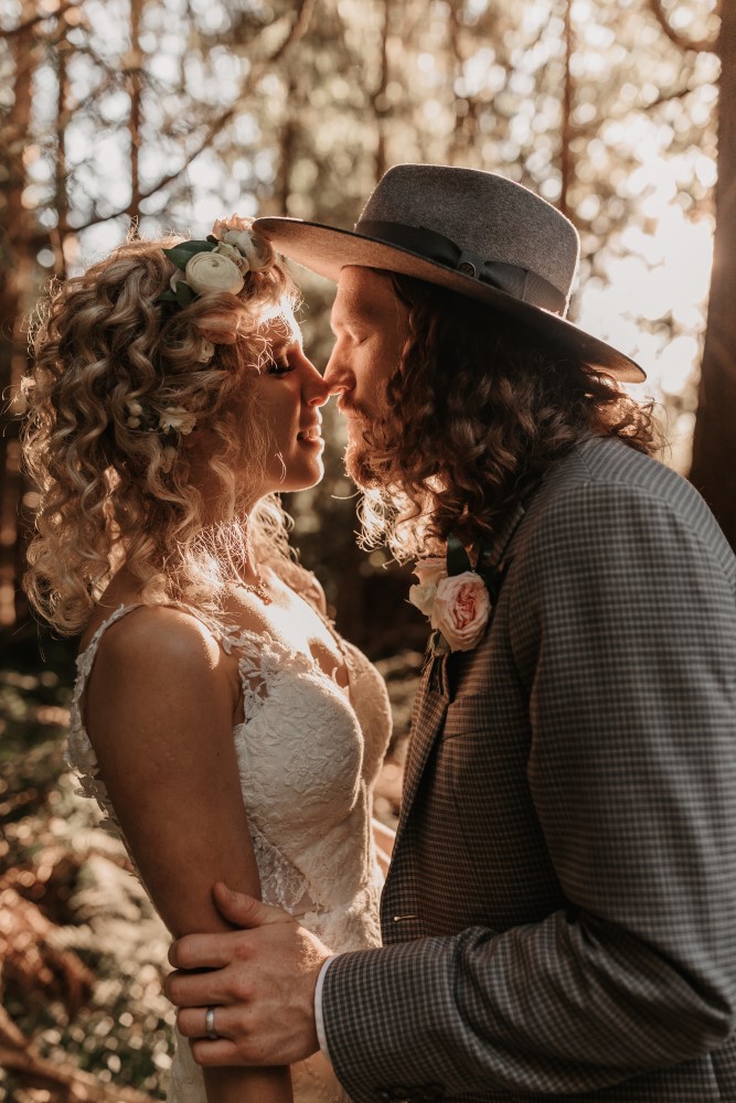 Golden Hour HAIR+ MUA Rainbow Room Hair Salon Bride and Groom going in for a kiss nose touching floral designs by Coastal Weddings & Events