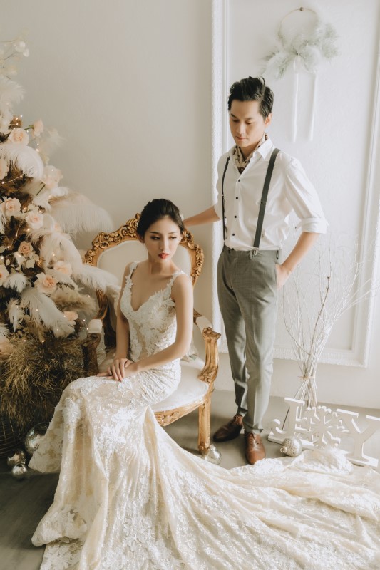 Dreamy White Wedding bride in lacy v-neck gown with long train sitting on chair with groom behind resting his hand on the chair's back