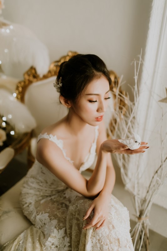 Dreamy White Wedding bride sitting on white and gold chair with hand out palm up holding a white bird