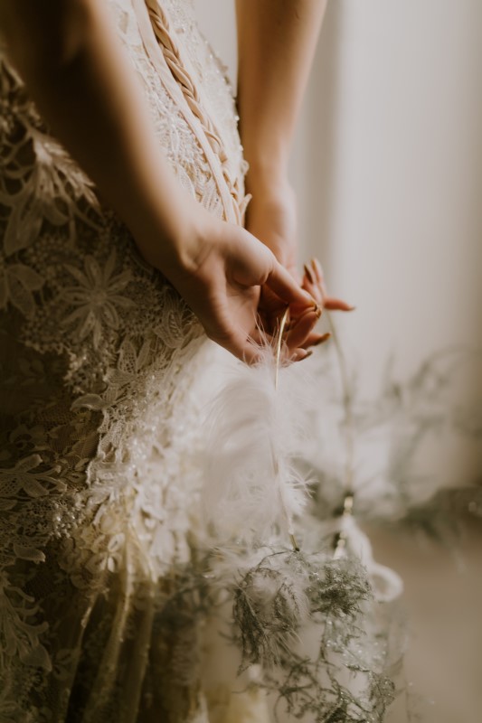 Dreamy White Wedding hands behind bride's back holding a feather