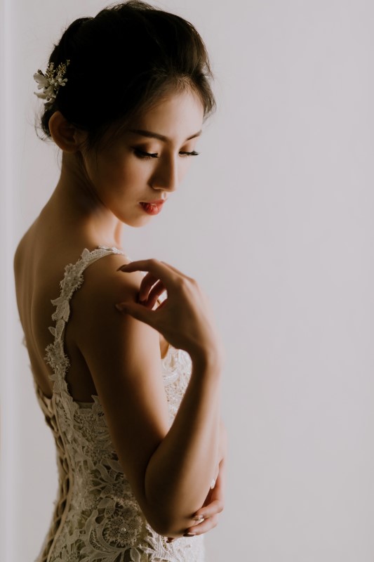 Dreamy White Wedding bride in lace gown touching her shoulder looking down