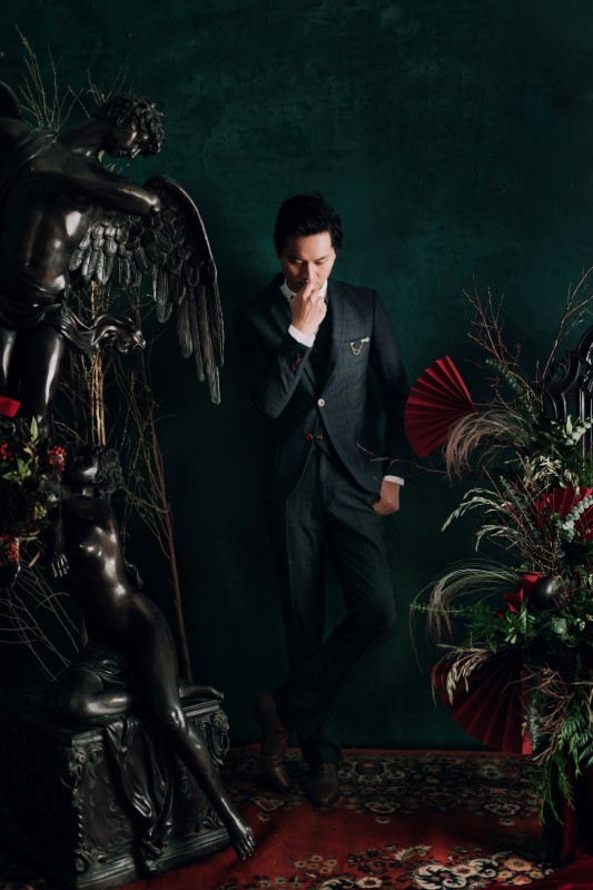 Culture Fusion groom thinking pose next to black angel statue and greenery arrangement