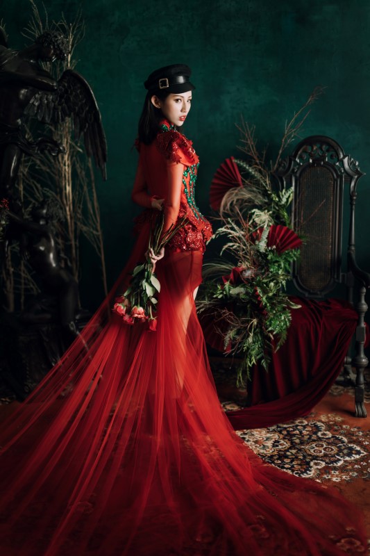 West Coast Weddings Magazine bride in red gown looking over her shoulder holdingm bouquet of red roses next to floral arrangement with red fans