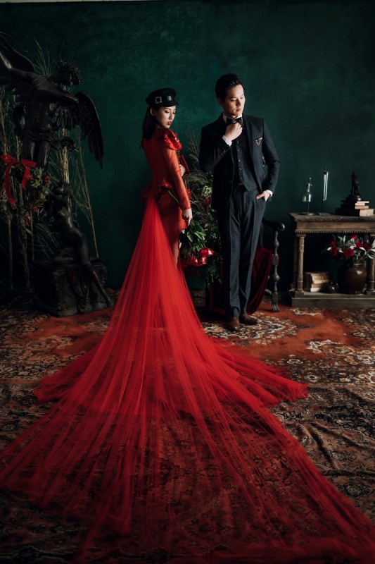 Culture Fusion bride in red dress with really long train laid out, groom next to her fixing his tie