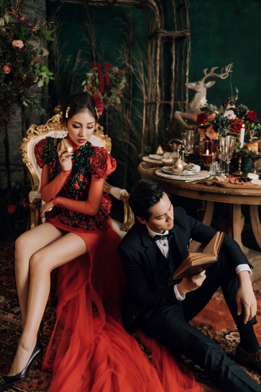 Culture Fusion bride in red dress sitting on chair looking down at groom sitting on the ground reading a book