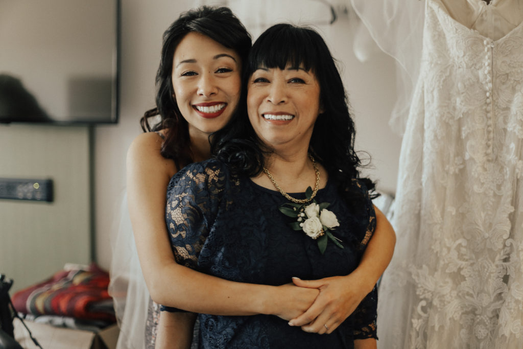 Steal of a Wedding bride hugging her mother from behind with makeup done by Erin Bradley