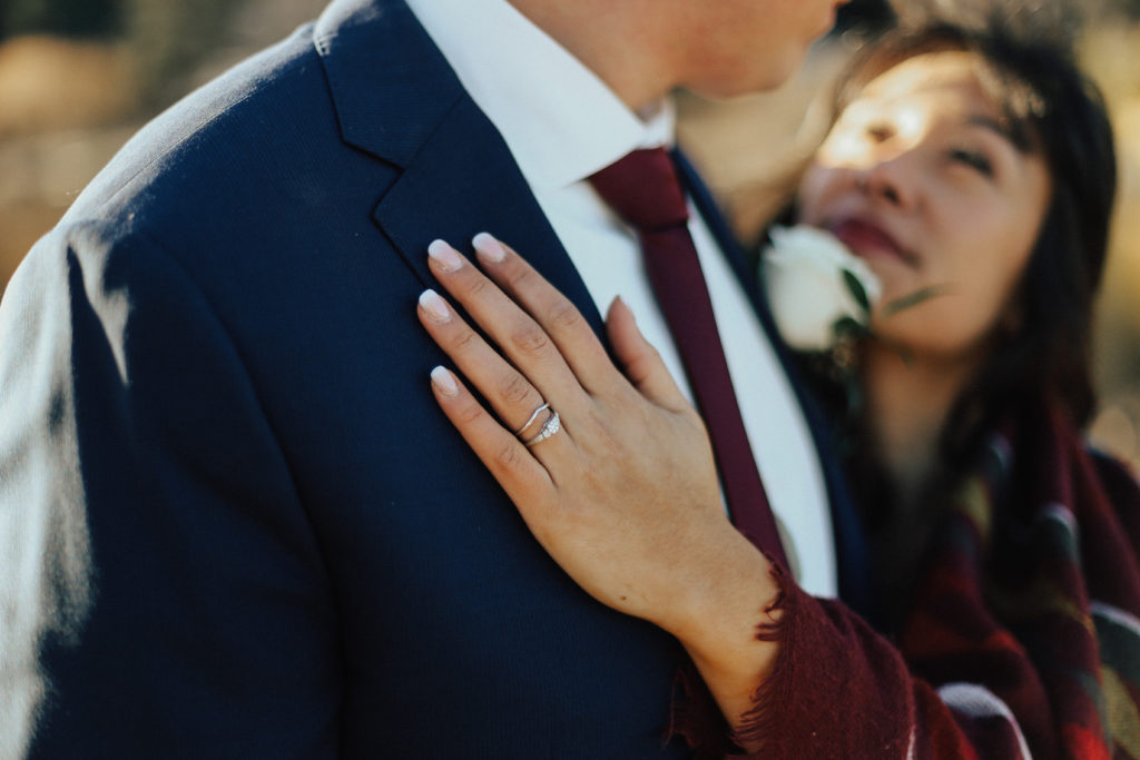 Steal of a Wedding bride's hand on groom's chest showing off wedding band and engagement ring from People's Jewellers