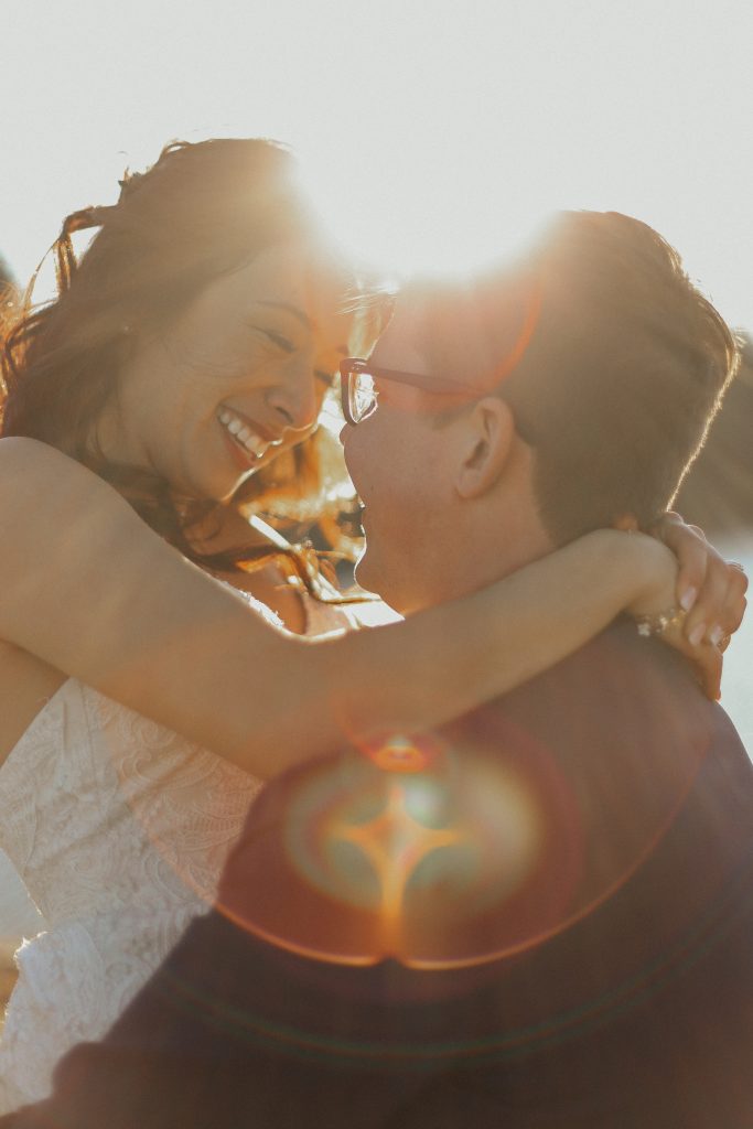 Steal of a Wedding groom holding up smiling bride with lens flare and sun in the background Jane Avenue Photography