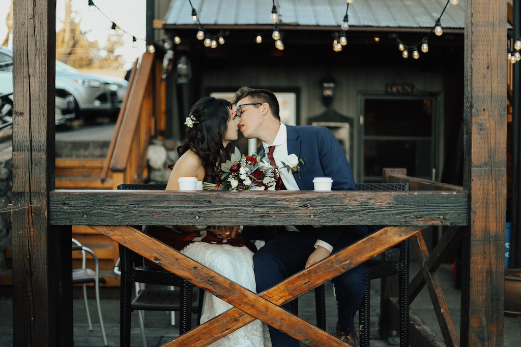 West Coast Weddings Magazine bride and groom kissing under string of lights at a coffee shop