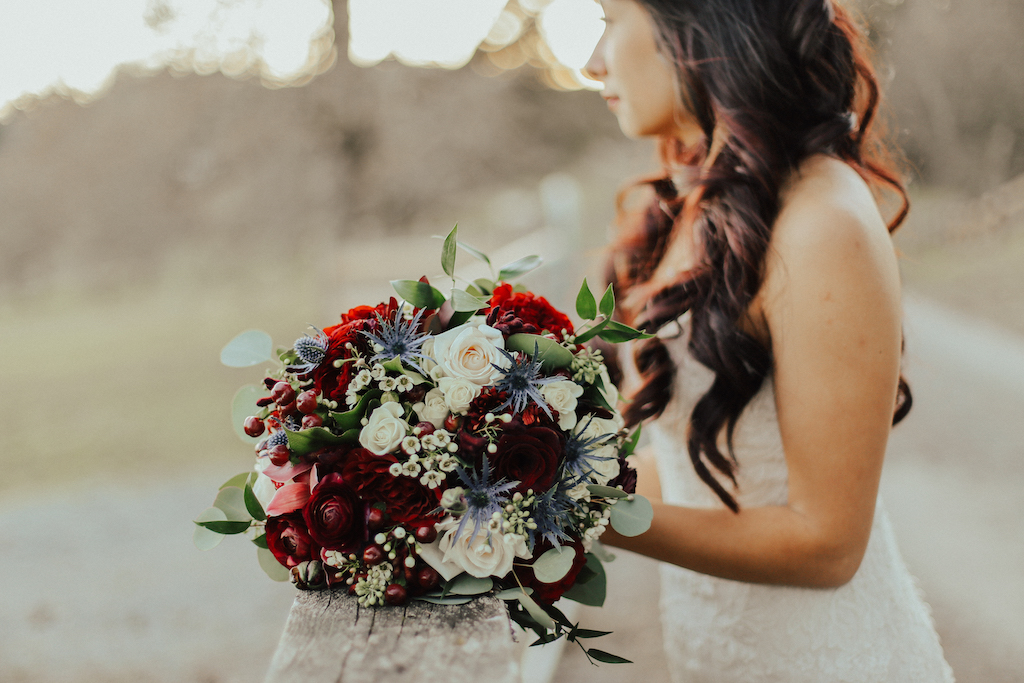 Steal of a Wedding bouquet resting on fence with red and blue flowers by West Coast Weddings Magazine and bride in the background 