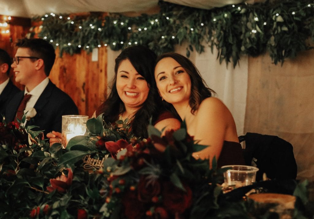 Steal of a Wedding bridesmaids sitting at head table with a lot of greenery and marsala roses