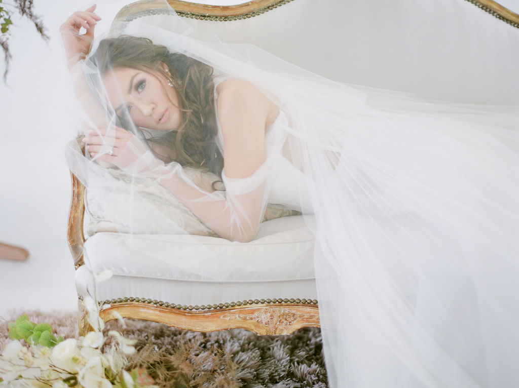 Simply Sweet Airside Space with bride laying on white settee under a veil by Vera Wang