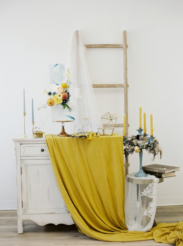 Vintage desk with yellow linen and dusty blue wedding cake and candles 