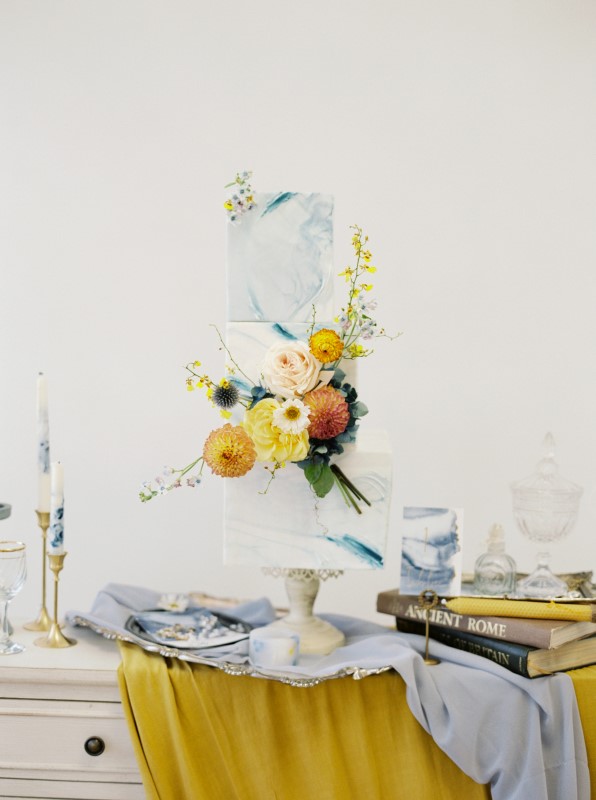 Three tier wedding cake with exquisite flowers surrounded by antique books and candles