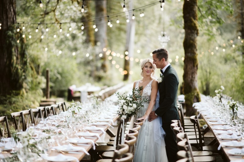 Newlyweds look over reception tables in the woods by Truffles Catering on Vancouver Island