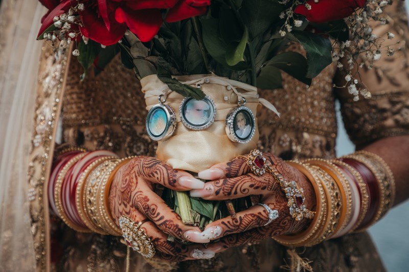 Bridal Bouquet with relatives photos attached held by hands covered in henna and gold bracelets