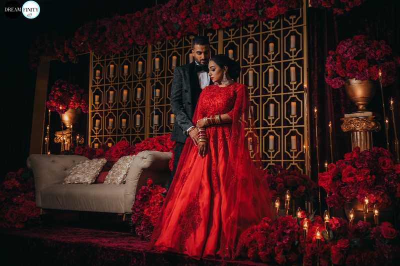 Flawless Bridal Fusion Newlyweds on Traditional Indian Dias covered in scarlet red roses and gold backdrop by Universal Decor Events