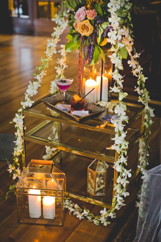 Bengal Spice white orchids strung over glass table and lit candles with Pink Cocktail 