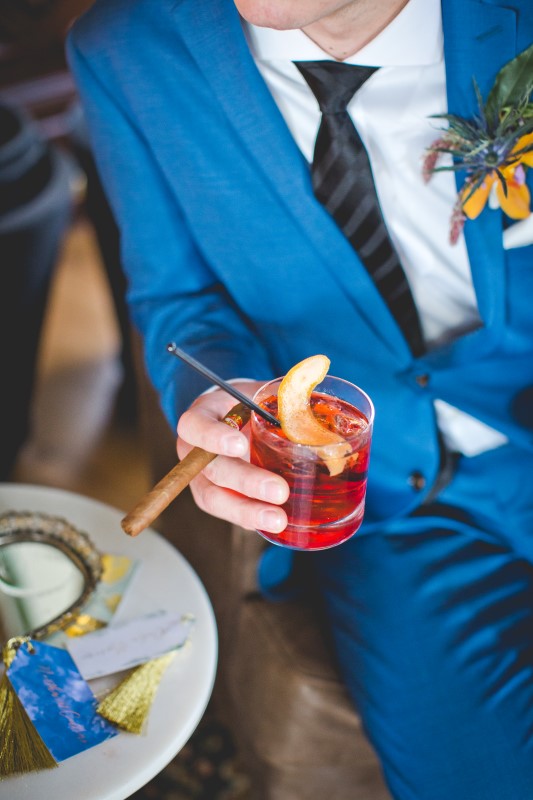 Cigar and Q Signature Drink at the Fairmont Empress held by groom wearing blue suit by Hughes Clothing