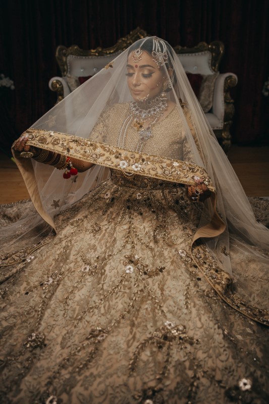 Indian Bride looking through gild edged veil by Pristine Allure Studio