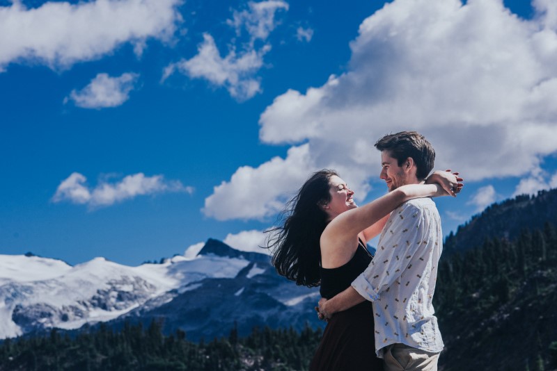 Engaged couple embrace in front of snow peaked Rocky Mountains